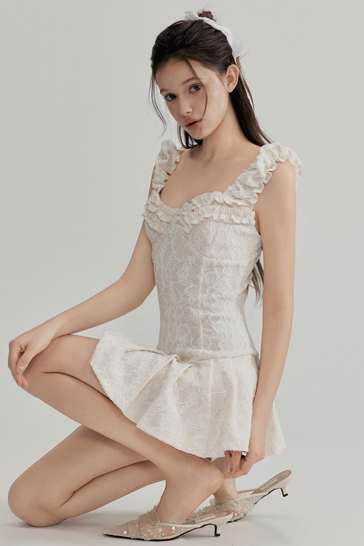 Woman wearing a white lace dress with floral details on a plain background