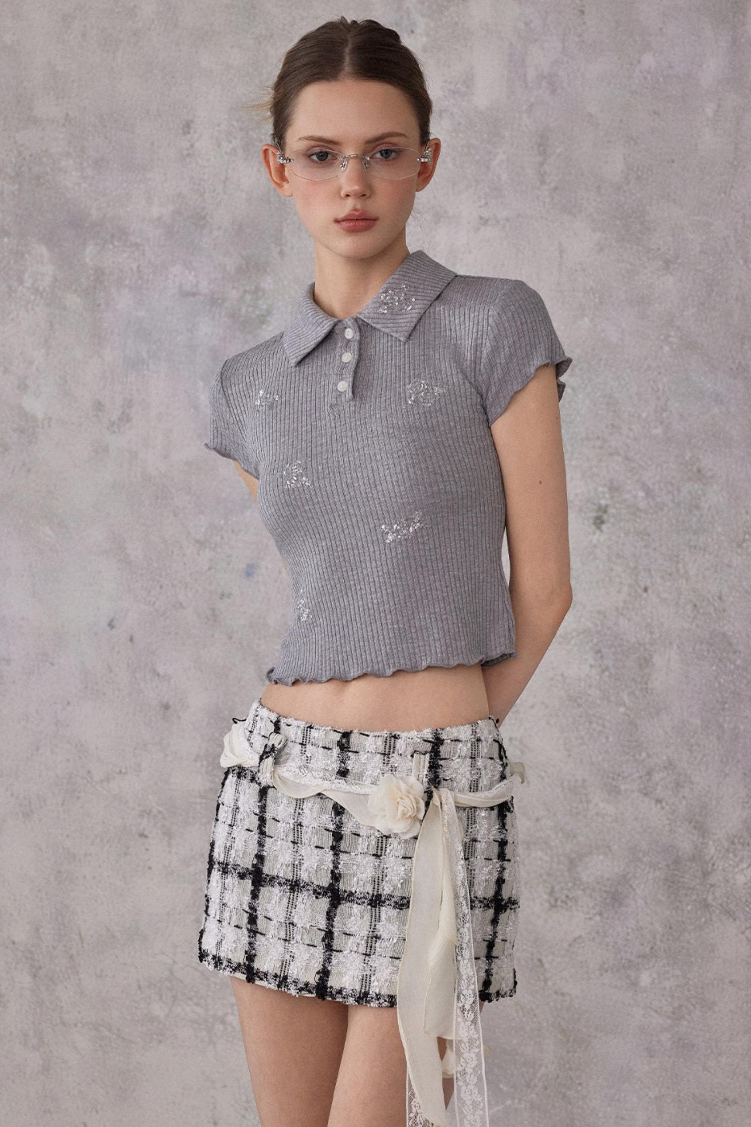 Woman wearing a gray patterned top and plaid skirt against a gray background