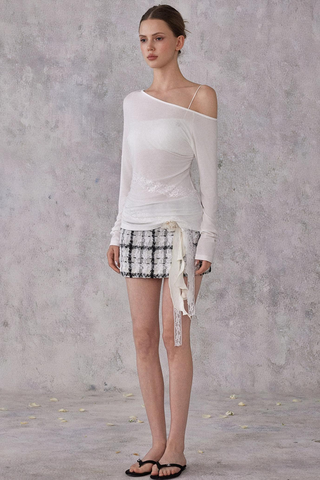 Woman wearing a white off-shoulder top and patterned shorts against a gray background