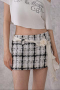Woman wearing a white one-shoulder top with text and a black and white checkered skirt against a gray background