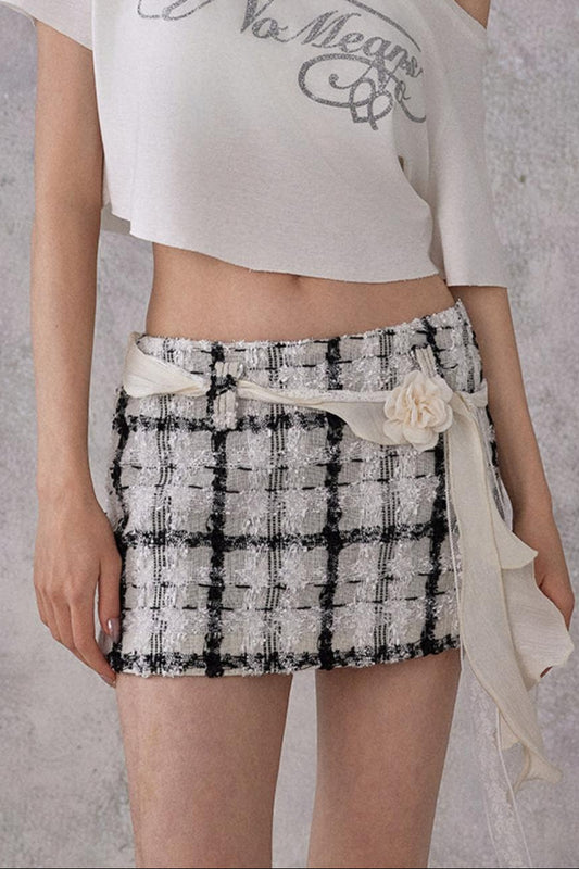 Woman wearing a white one-shoulder top with text and a black and white checkered skirt against a gray background