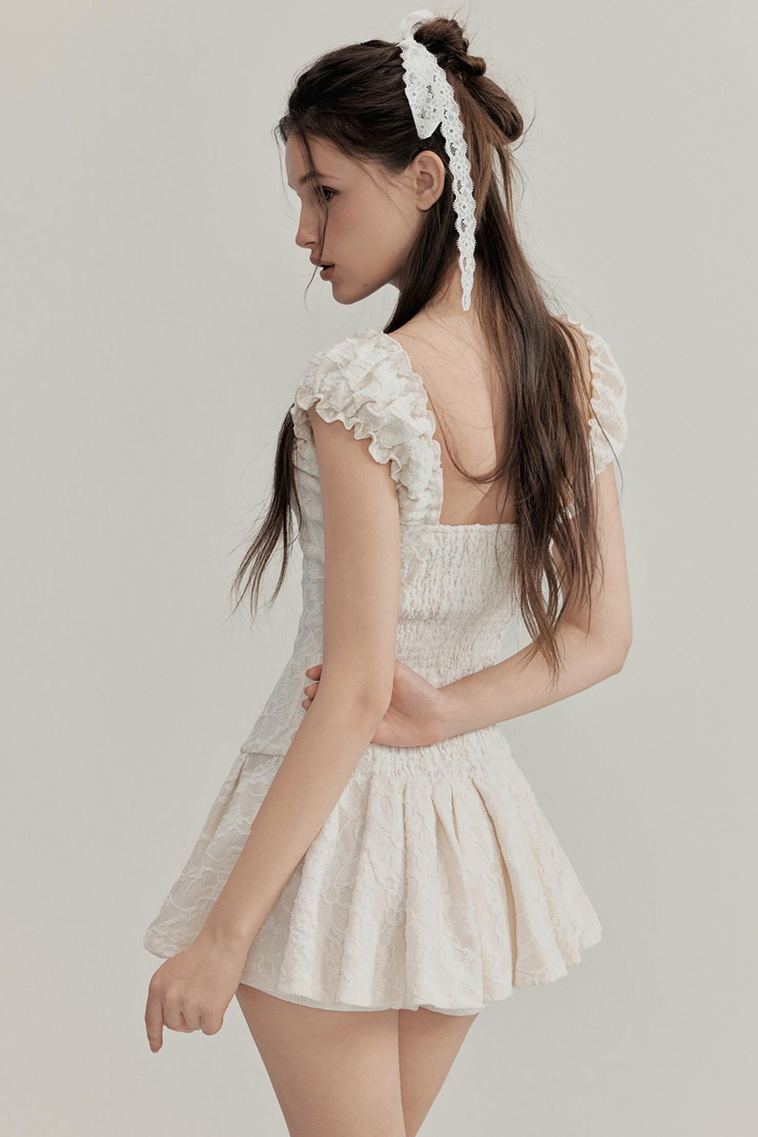 Young girl wearing a white lace dress against a plain background