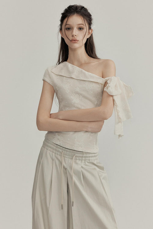 Woman wearing a beige one-shoulder top and pants against a plain background