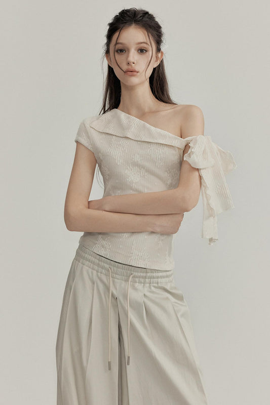 Woman wearing a beige one-shoulder top and pants against a plain background