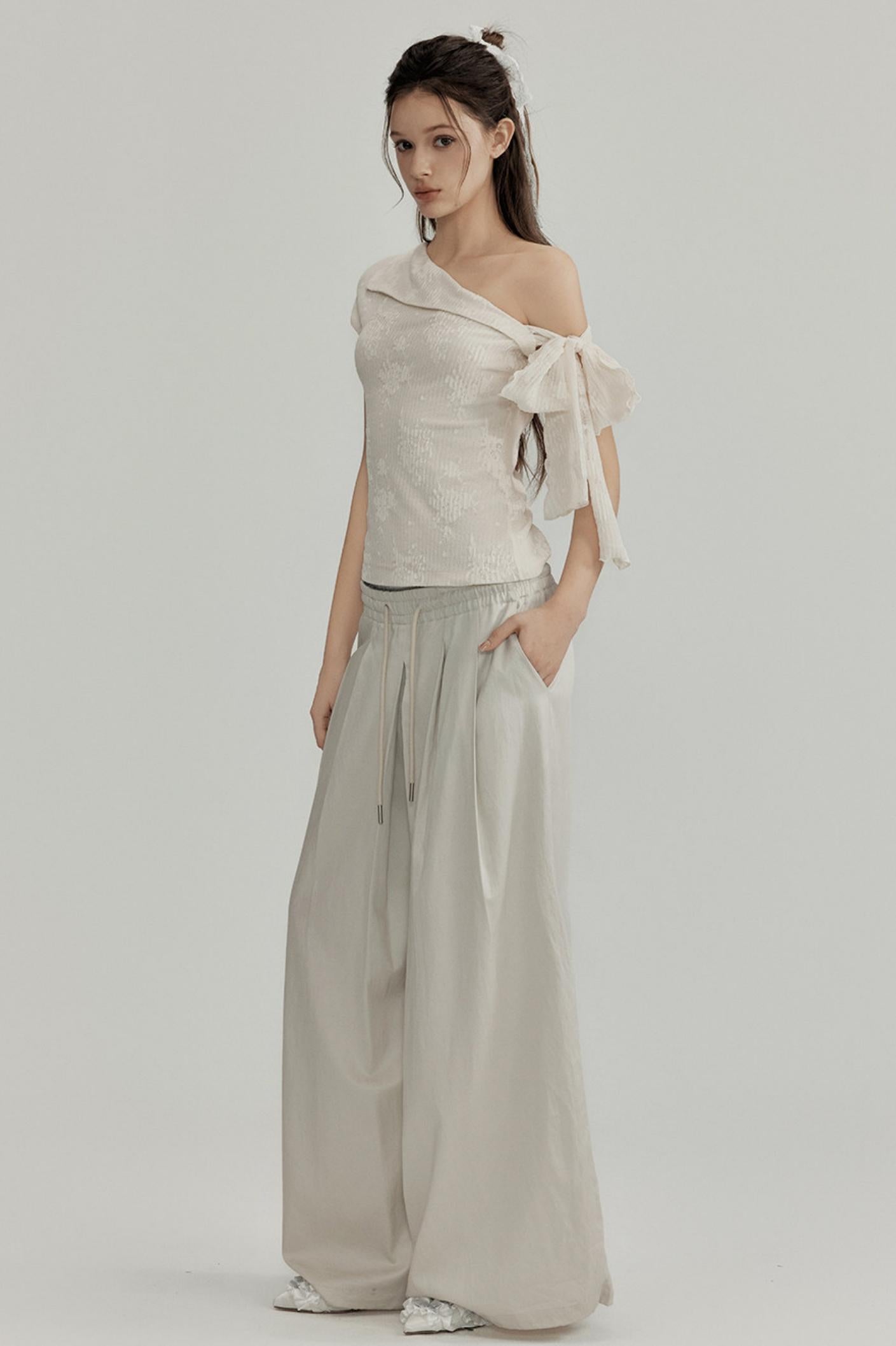 Woman wearing a one-shoulder top with a bow and wide-leg pants on a plain background