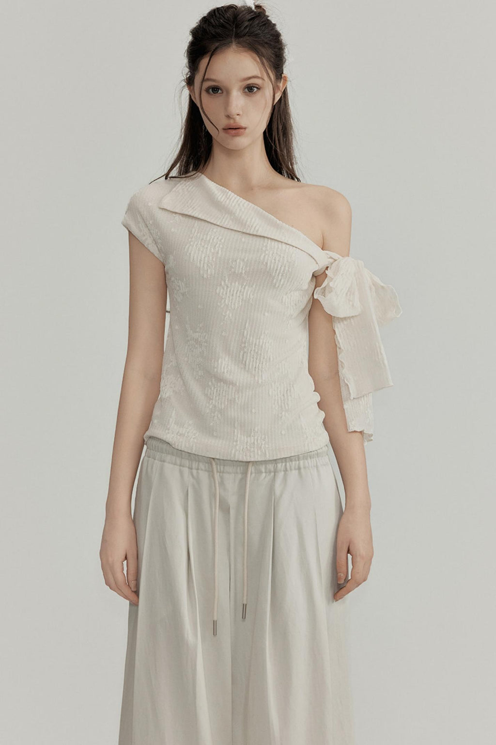 Woman wearing a one-shoulder beige top with a plain background
