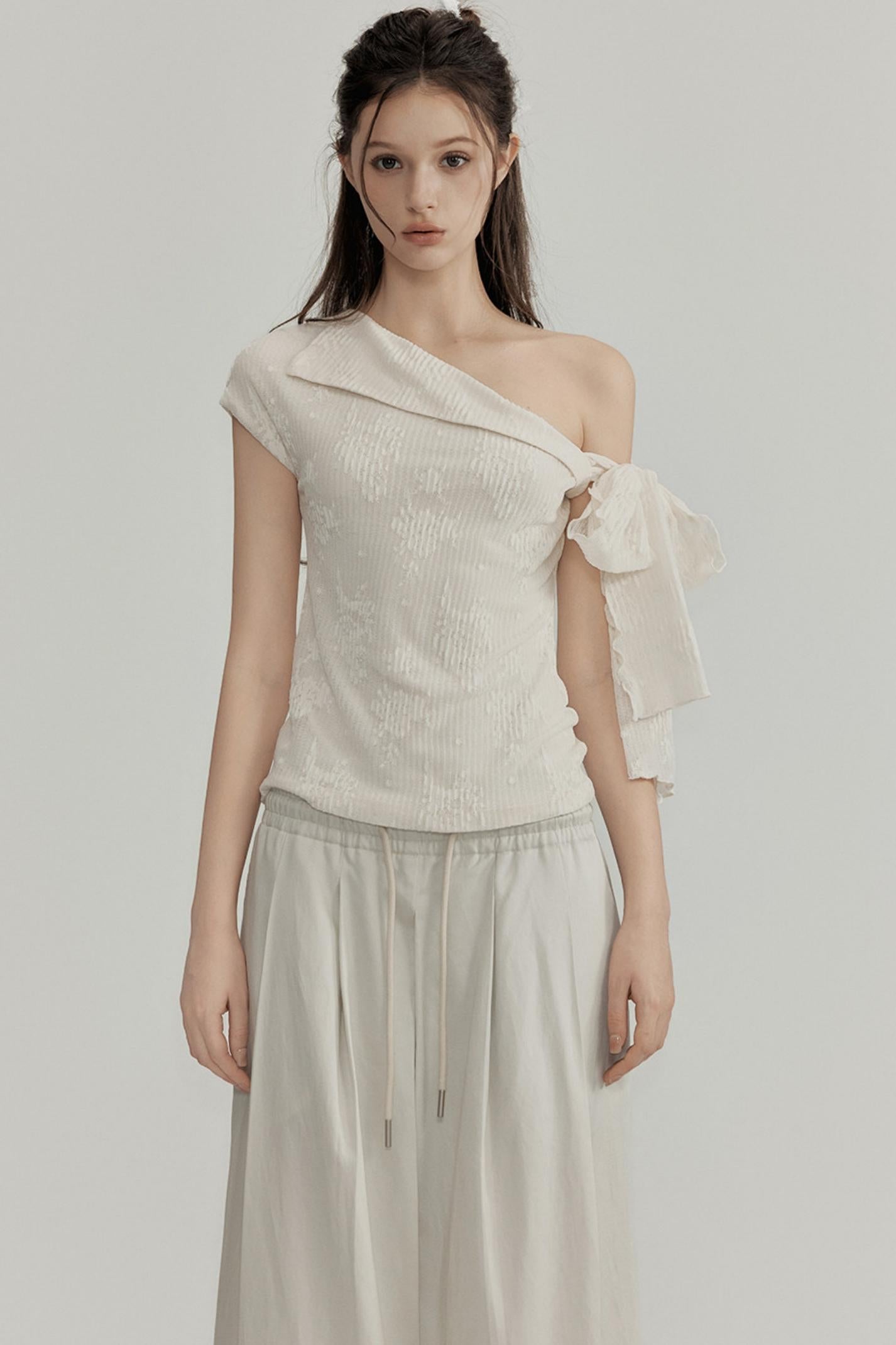 Woman wearing a one-shoulder beige top with a plain background