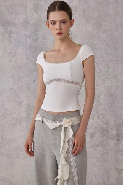 Woman wearing a white top with lace details and gray pants against a gray background