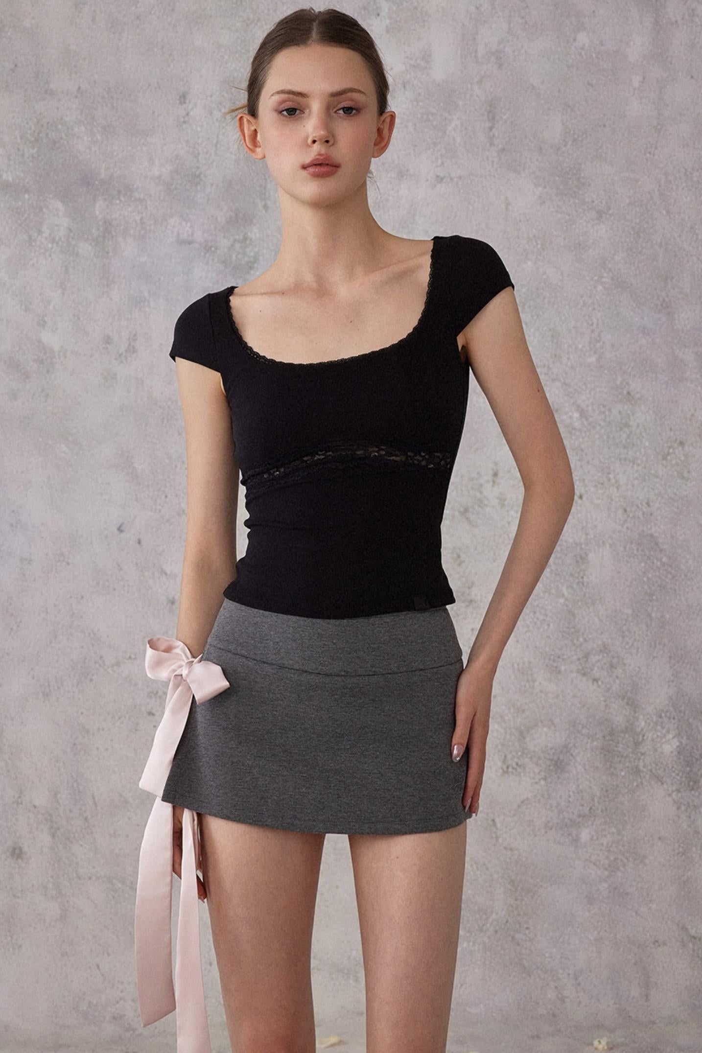 Woman wearing a black top and gray skirt against a gray background