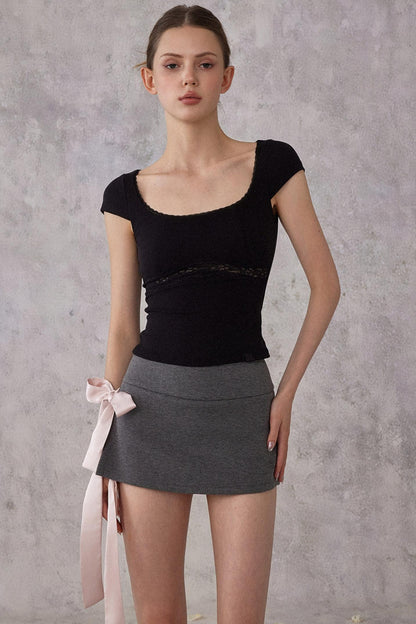 Woman wearing a black top and gray skirt against a gray background
