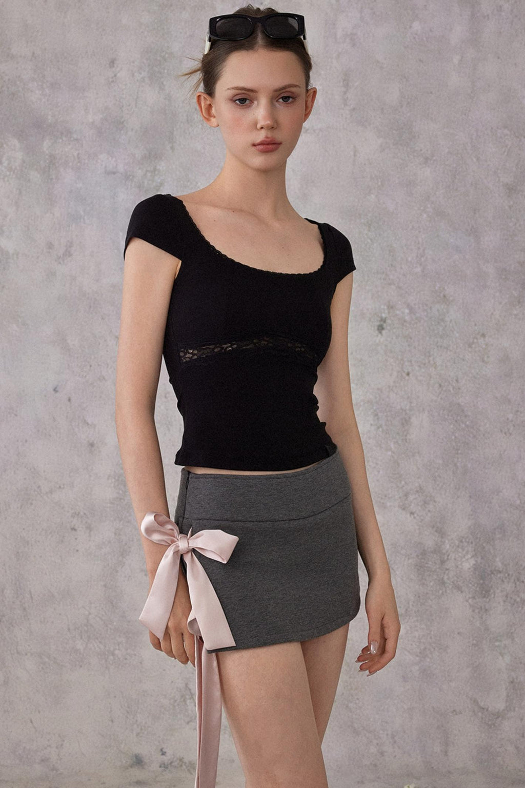 Woman wearing a black top and gray skirt with a pink ribbon against a gray background
