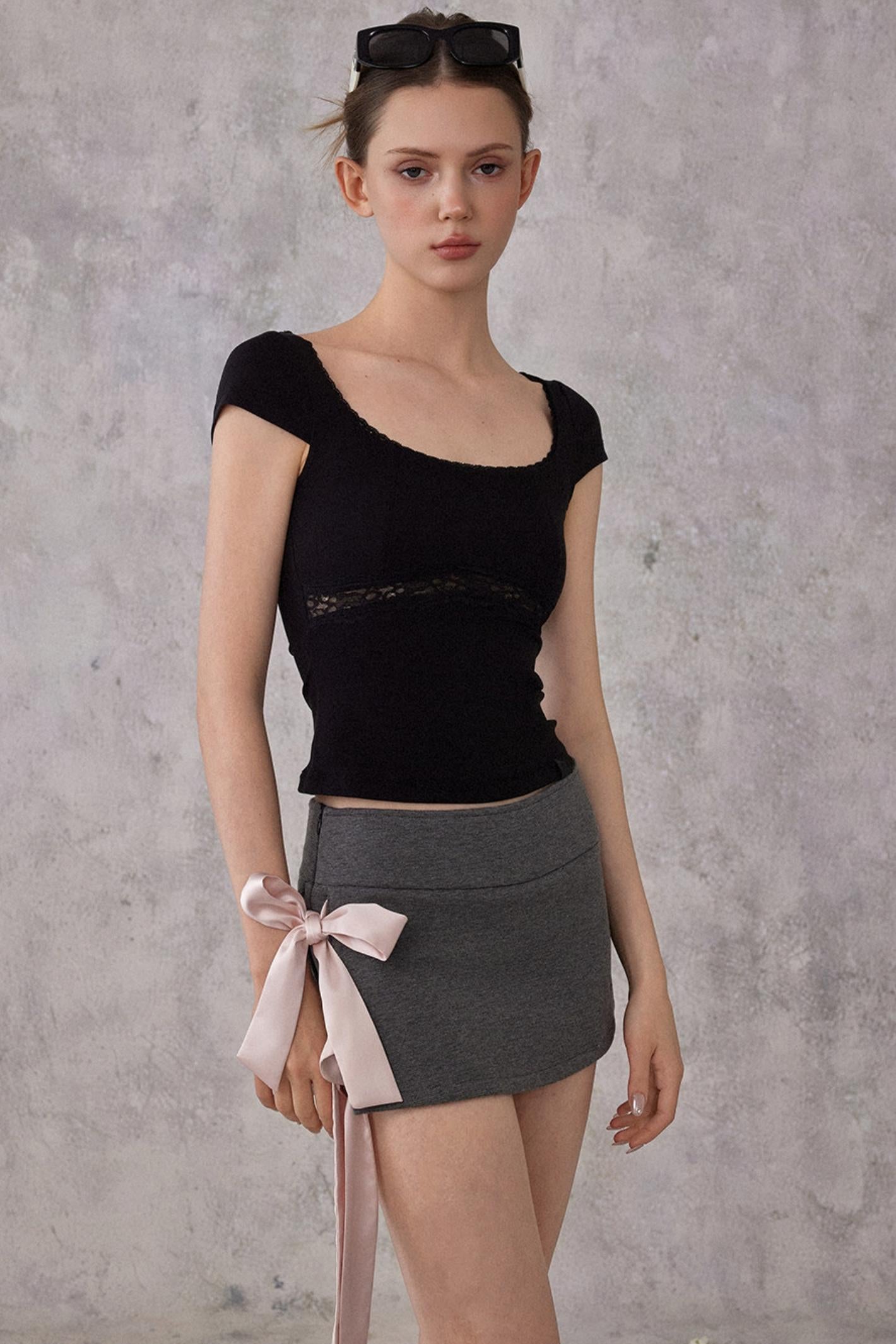 Woman wearing a black top and gray skirt with a pink ribbon against a gray background
