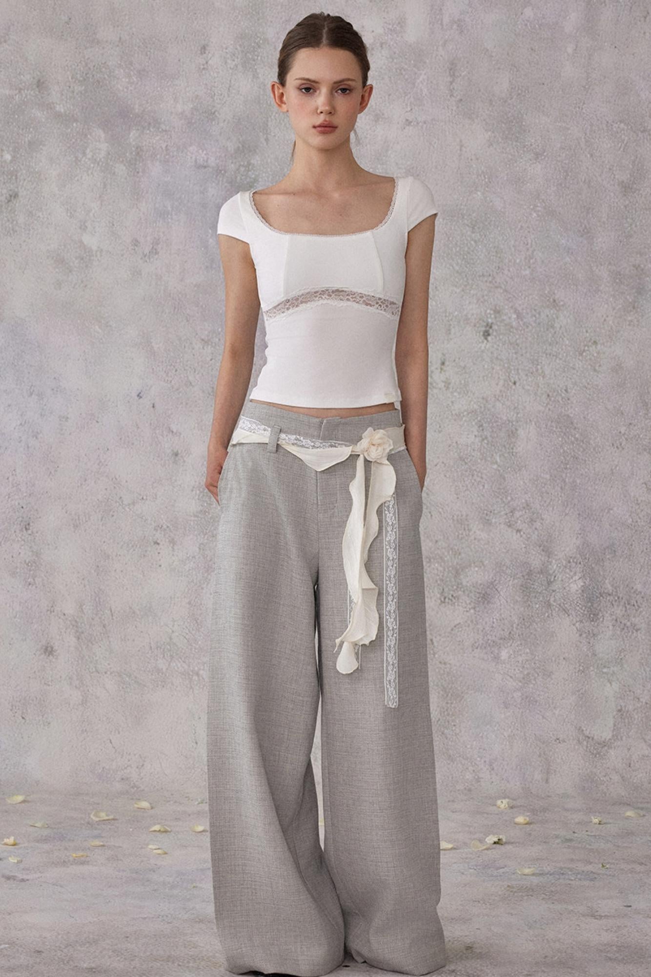 Woman wearing a white top and gray pants with a belt against a plain background