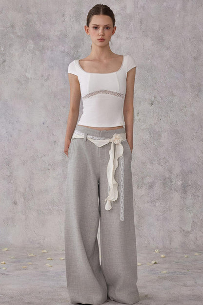 Woman wearing a white top and gray pants with a belt against a plain background