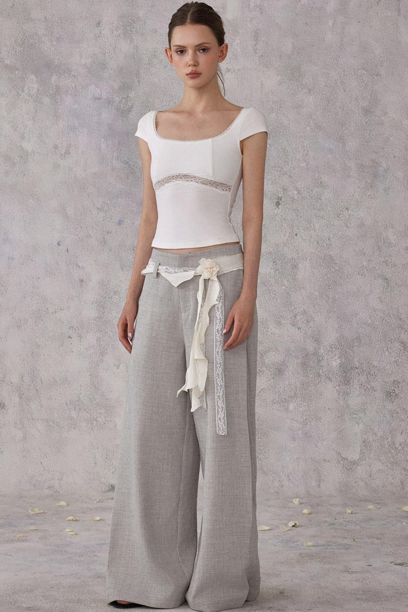 Woman wearing a white top and gray wide-leg pants against a plain background