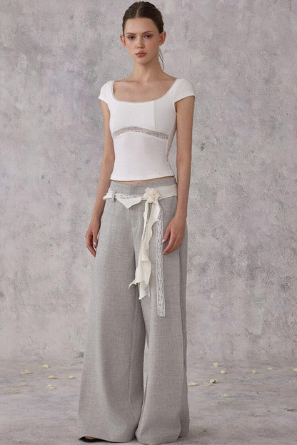Woman wearing a white top and gray wide-leg pants against a plain background