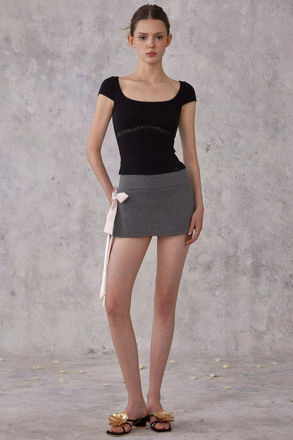 Woman wearing a black top and gray skirt against a gray concrete wall.