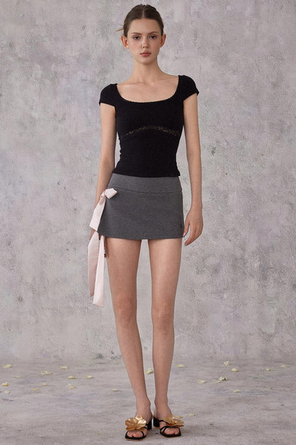 Model wearing a black top and gray skirt against a gray background