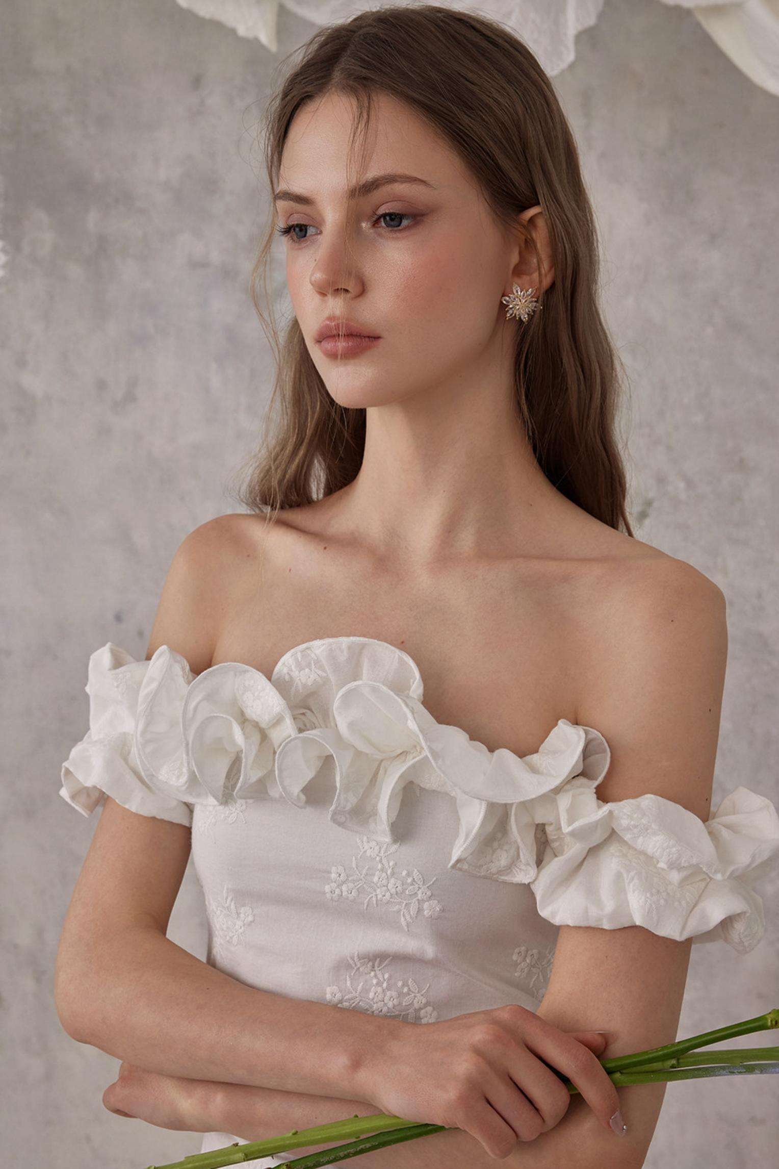 Woman wearing a white off-shoulder dress with ruffled sleeves against a neutral background