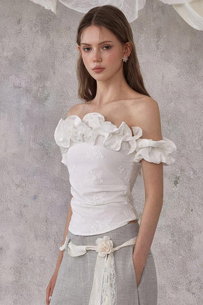 Woman wearing a white strapless top with floral details against a gray background