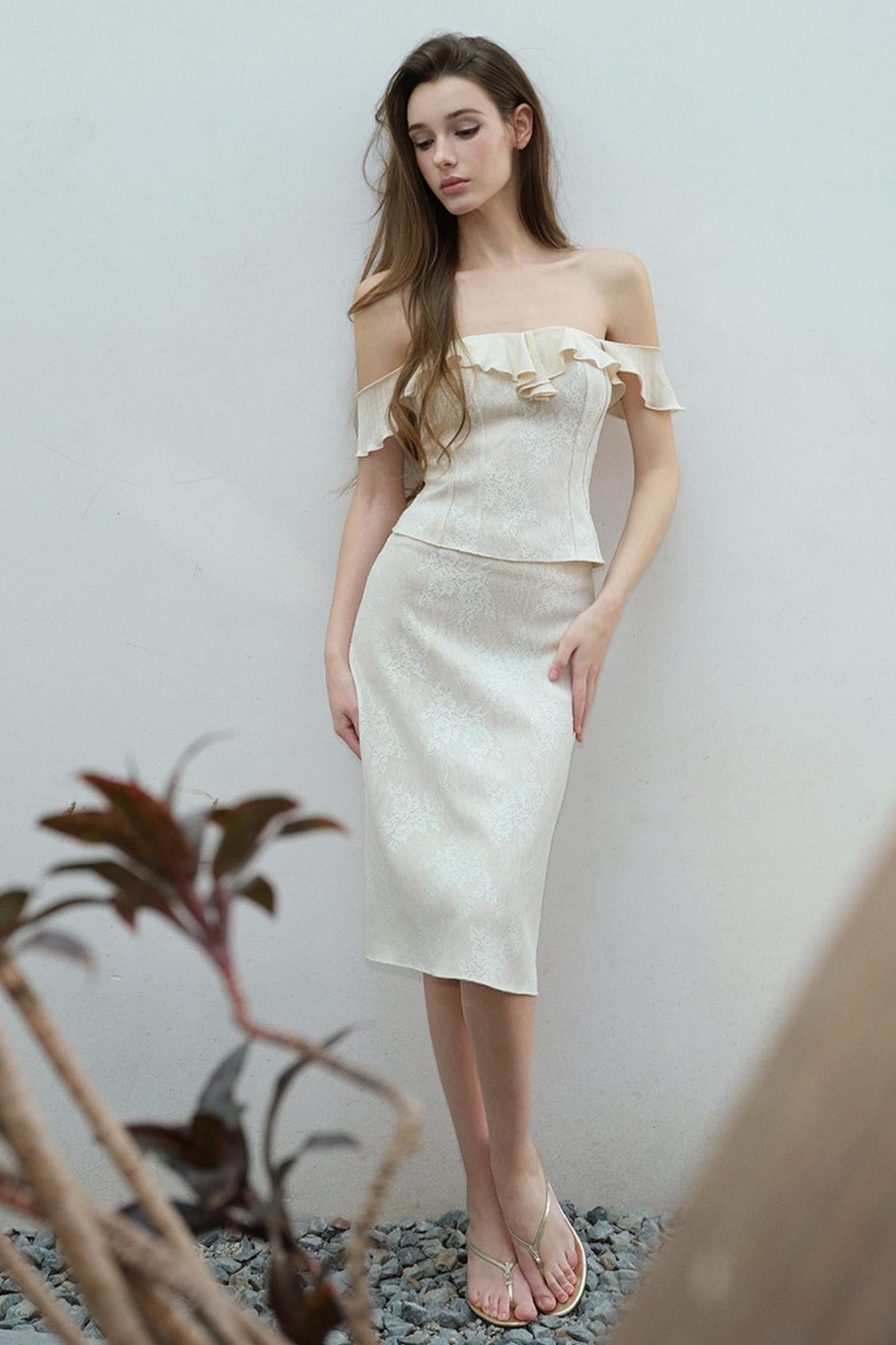 Woman wearing a white off-shoulder dress standing against a plain background