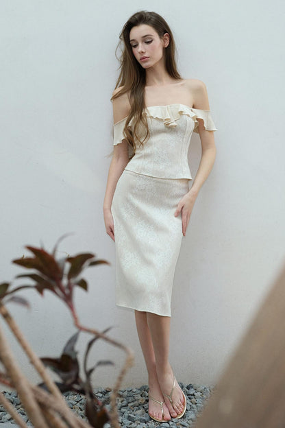 Woman wearing a white off-shoulder dress standing against a plain background