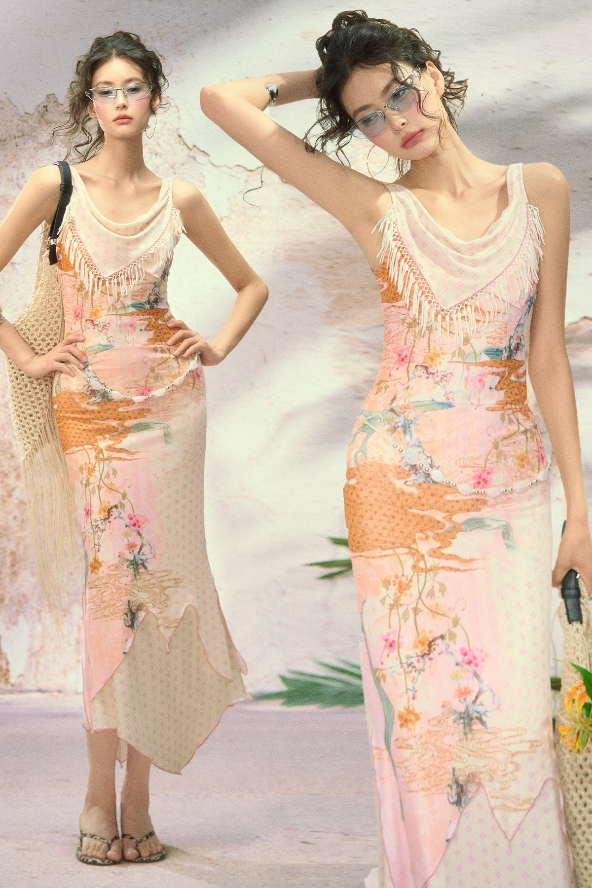 Two models wearing matching light pink and beige maxi dresses with a watercolor-style floral and landscape print, standing against a textured beige wall.