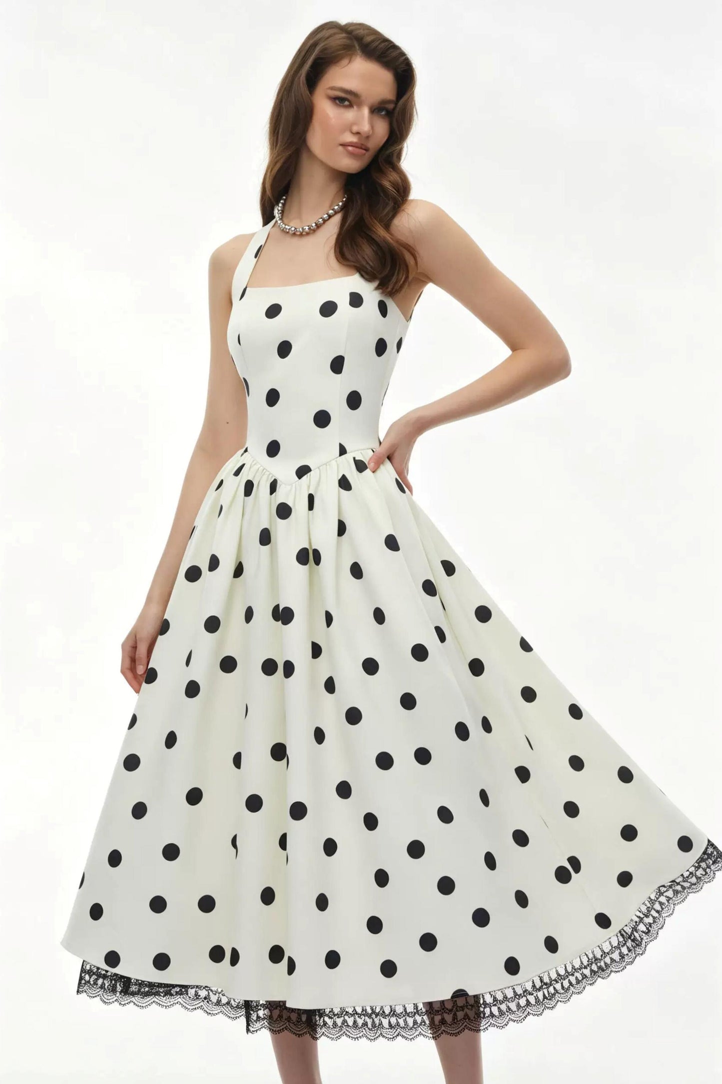 A woman modeling a sleeveless white dress with large black polka dots and a flared skirt against a plain white studio background.