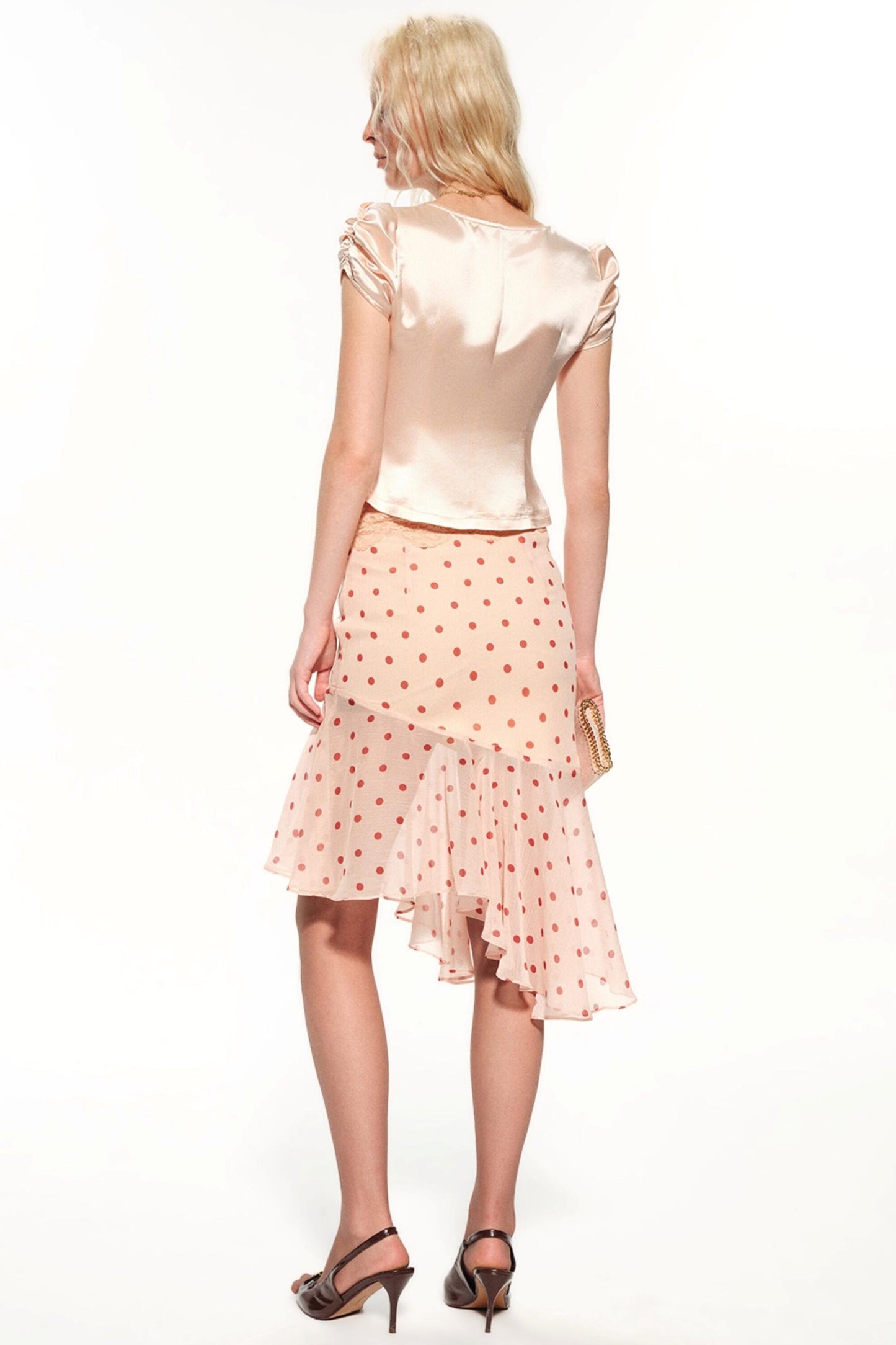 A woman shown from the back wearing a pale peach satin short-sleeve top and a matching light pink polka-dot ruffled skirt, paired with dark heeled sandals against a plain white studio background.