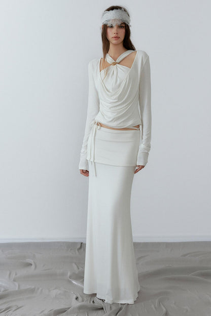 Woman wearing a white dress with long sleeves and a headband against a plain background