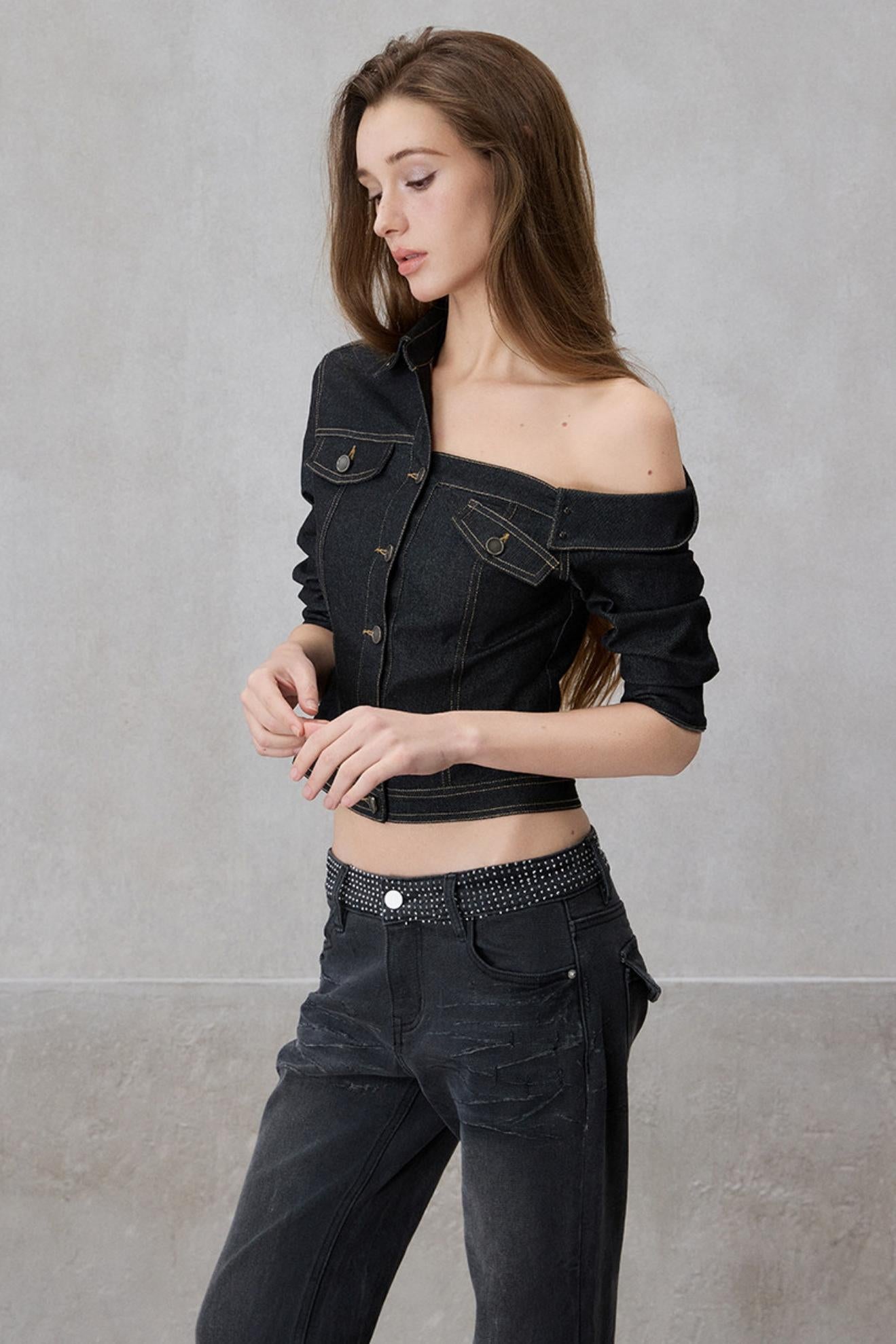 Woman wearing a black denim jacket and jeans against a gray background