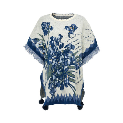 A cream-colored knit poncho sweater featuring a blue and green floral pattern, fringed edges, and pom-poms at the bottom, displayed on a white background.