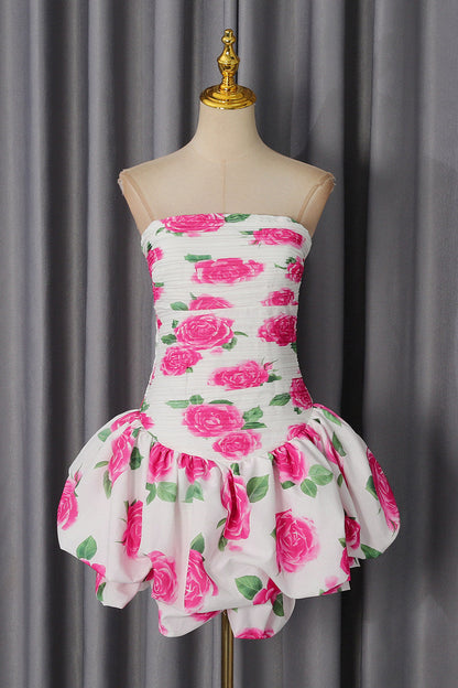 A strapless white dress with a vibrant pink rose and green leaf pattern, displayed on a beige mannequin dress form against a gray curtain backdrop.
