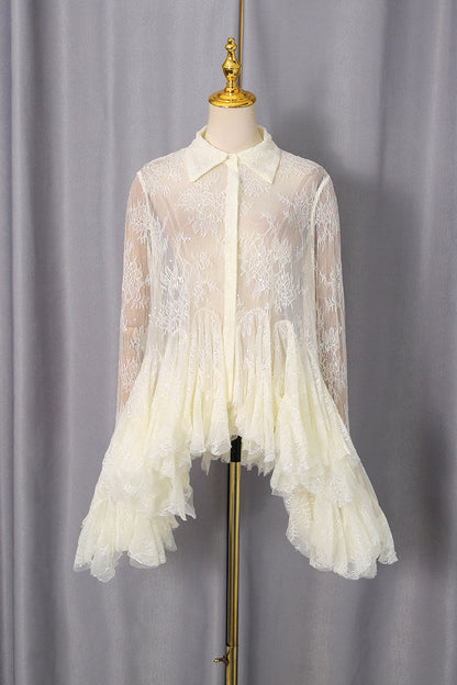 An ivory lace long-sleeve blouse with a ruffled tiered hem, displayed on a cream mannequin torso with a gold stand against a gray curtain backdrop.