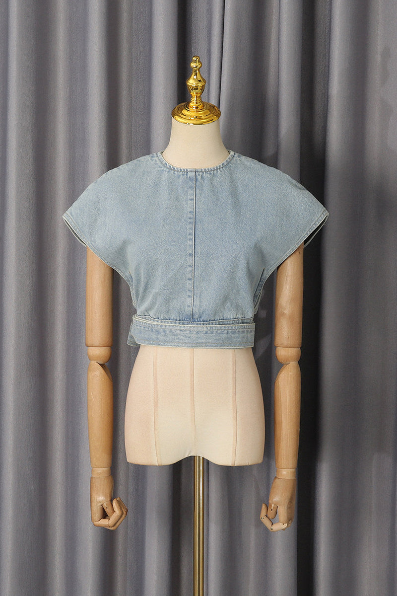 A light blue cropped denim top with short wide sleeves and a buttoned center back, displayed on a beige mannequin torso against a gray curtain backdrop.