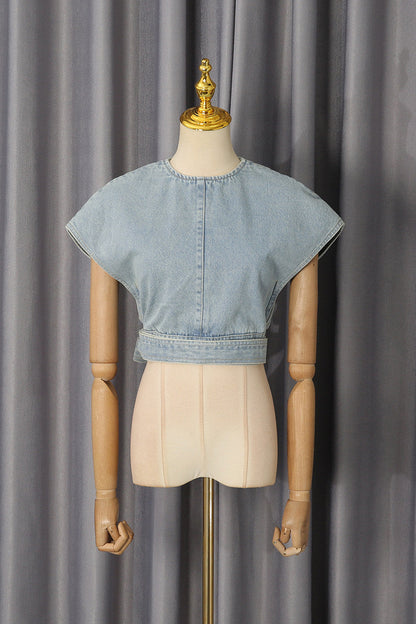A light blue cropped denim top with short wide sleeves and a buttoned center back, displayed on a beige mannequin torso against a gray curtain backdrop.