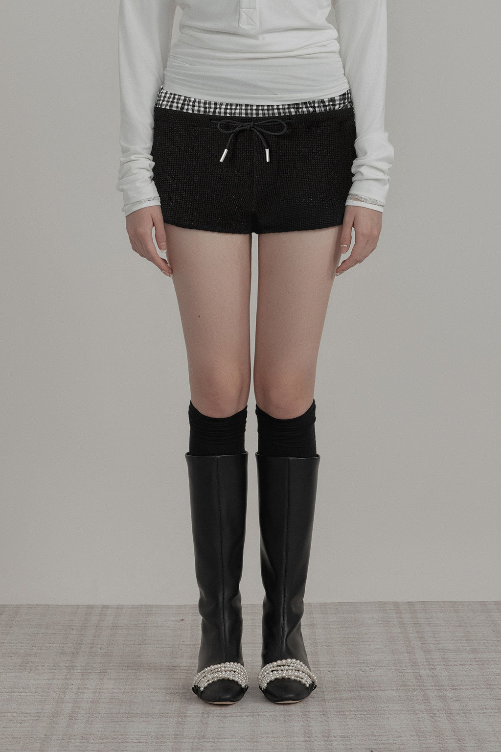 Person wearing black knee-high boots with decorative tops on a plain background