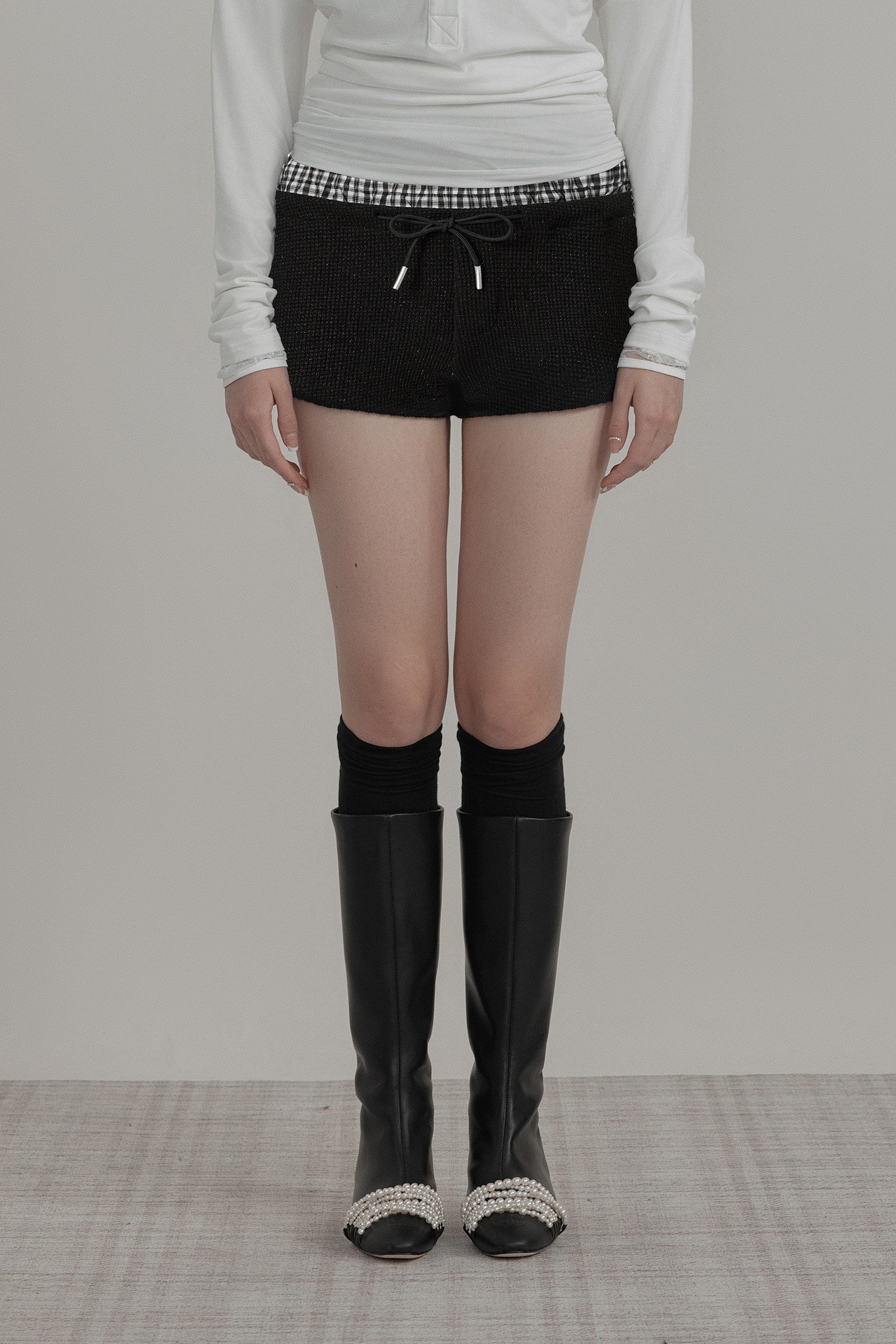 Person wearing black knee-high boots with decorative tops on a plain background