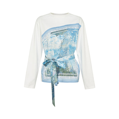 A white long-sleeve top with a wrap-style front panel featuring a blue landscape print and a matching blue tie belt, shown on a plain white background.