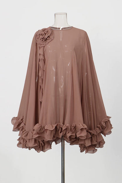 A dusty rose chiffon cape-style top with a large fabric flower detail on the shoulder, displayed on a mannequin against a light gray background.