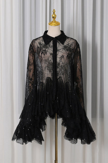 A black sheer lace blouse with a pointed collar, long sleeves, and a ruffled tiered hem embellished with small sequins, displayed on a mannequin torso against a white curtain backdrop.