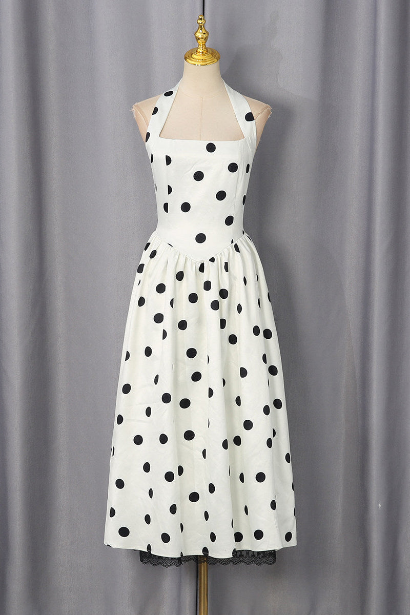 A white halter-neck dress with black polka dots, displayed on a mannequin against a gray curtain backdrop.