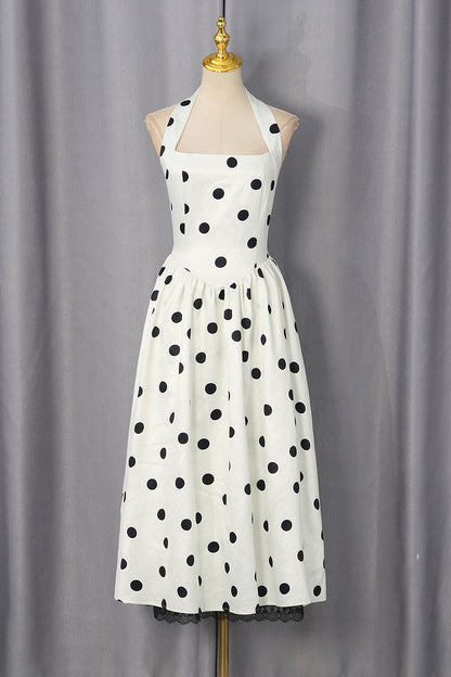 A white halter-neck dress with black polka dots, displayed on a mannequin against a gray curtain backdrop.