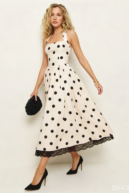A woman models a sleeveless midi dress with a black polka dot pattern on a cream background, featuring a lace hem and holding a black textured clutch against a plain light background.