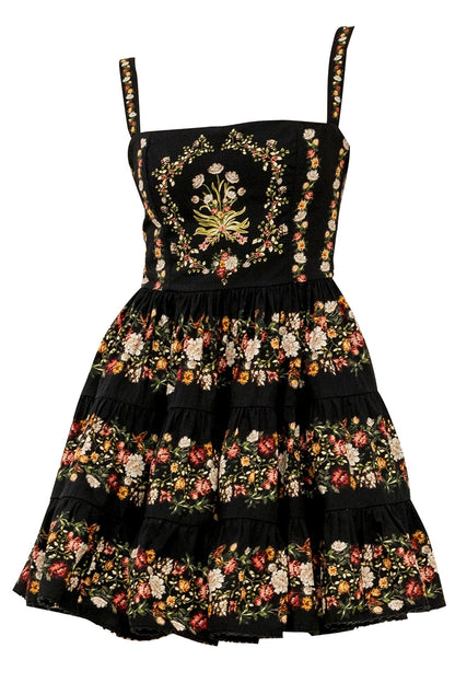 A black sleeveless dress with floral embroidery and a tiered skirt, featuring a central floral crest on the bodice and matching floral trim along the straps and edges.