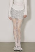 Person wearing a sparkly silver skirt and sheer white stockings against a plain background