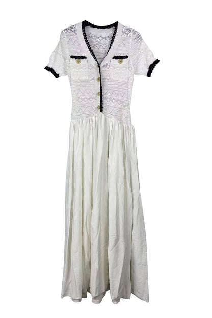 A white maxi dress featuring a textured crochet bodice with black trim, short sleeves with black cuffs, and a gathered skirt, displayed against a solid white background.