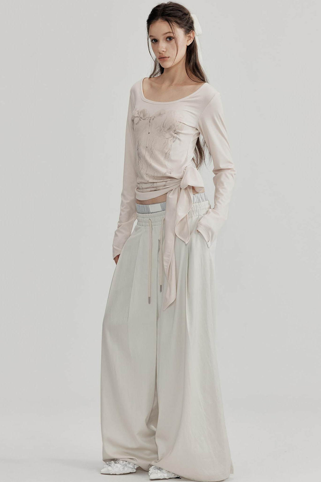 Woman wearing a beige long-sleeve top and wide-leg pants on a white background