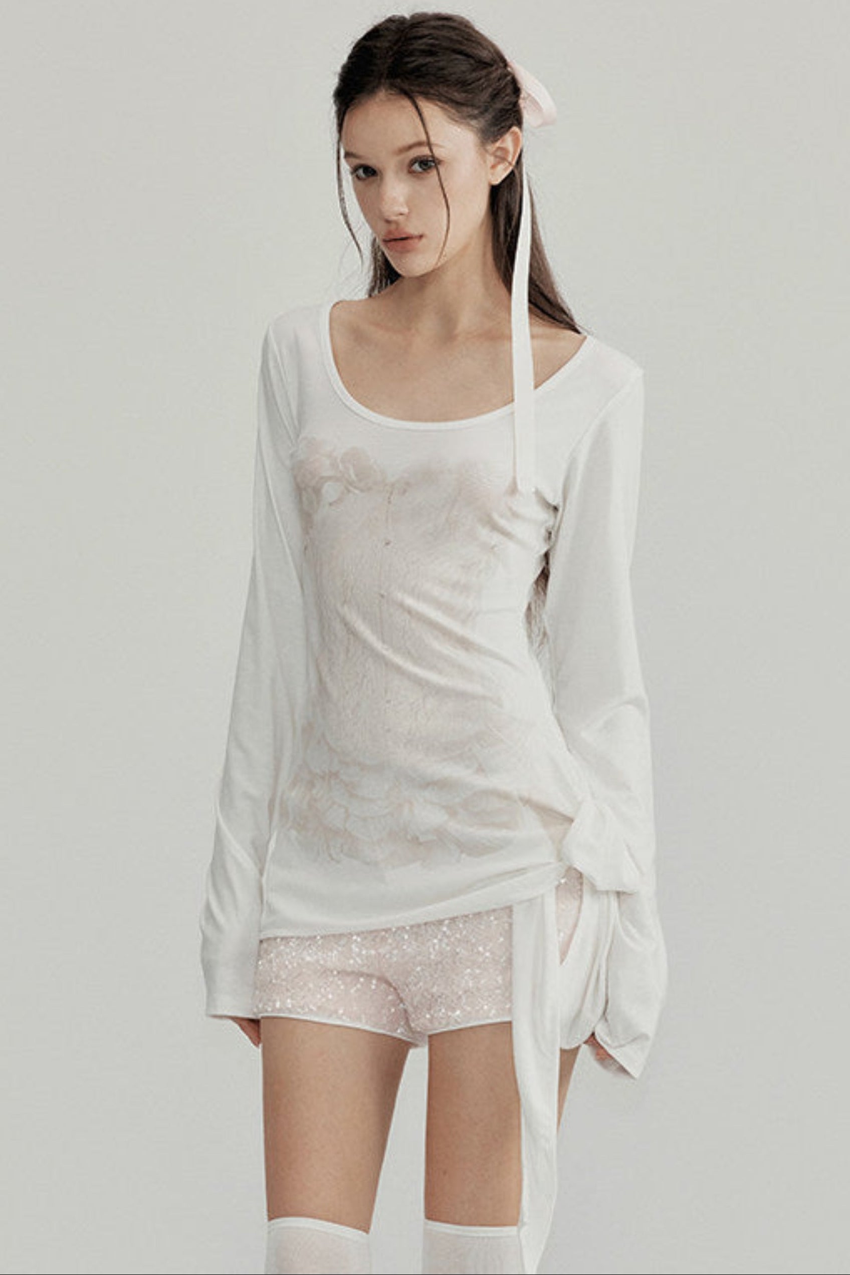 Woman wearing a white outfit with sheer elements on a plain background