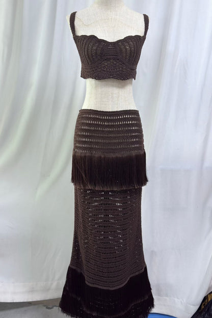A dark brown crocheted two-piece set displayed on a dress form, featuring a cropped tank top and a long tiered skirt with fringe details, set against a white curtain backdrop.